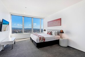 A hotel room with a large window, a bed, a desk, and a lamp.