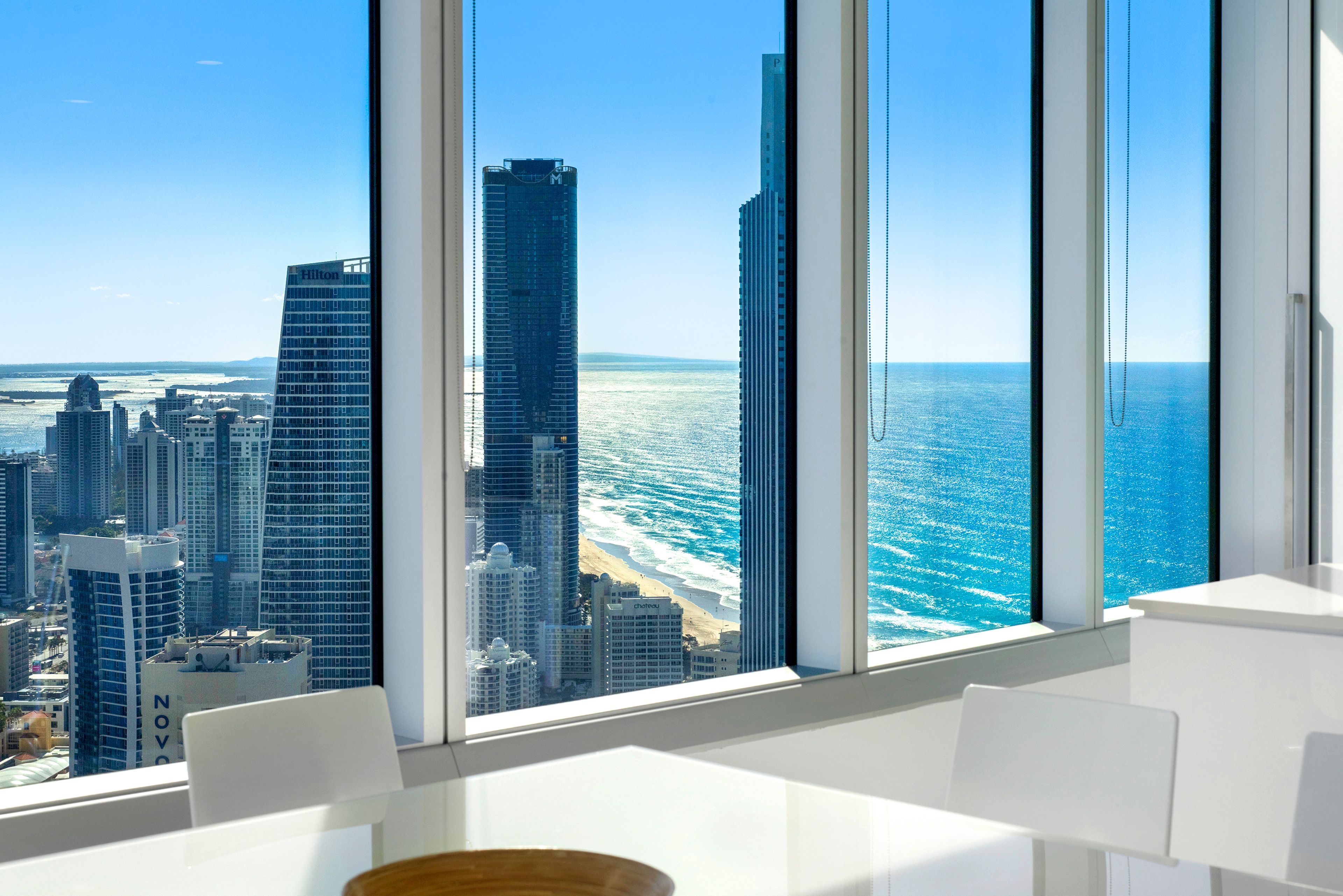 A modern hotel room with large windows overlooking a city skyline and a beach.