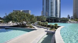 A modern hotel with a swimming pool, palm trees, and high-rise buildings in the background.