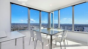 A modern dining room with a glass table and white chairs, large windows offering a city view. - Stunning 2 Bedroom Ocean Views Apartment - CoastHM (Surfers Paradise)