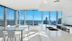 A modern kitchen with a city view, large windows, and a dining area with a table and chairs. - Stunning 2 Bedroom Ocean Views Apartment - CoastHM (Surfers Paradise)