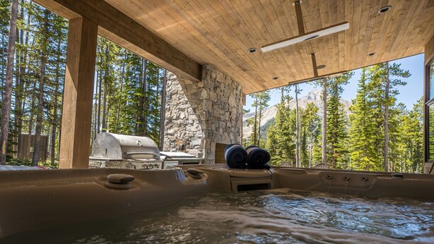 Un bain à remous dans un chalet en bois, avec un mur en pierre et une vue sur une forêt.