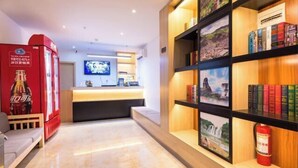A hotel lobby with a reception desk, a television, a bookshelf with books, and a fire extinguisher. - 24 Hours Banxing Hotel (Guiyang)