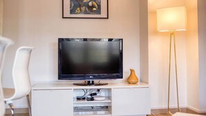 Ein modernes Wohnzimmer mit einem Flachbildfernseher auf einer weißen Unterhaltungseinheit, einem gerahmten Kunstwerk darüber und einer Stehlampe auf der rechten Seite.