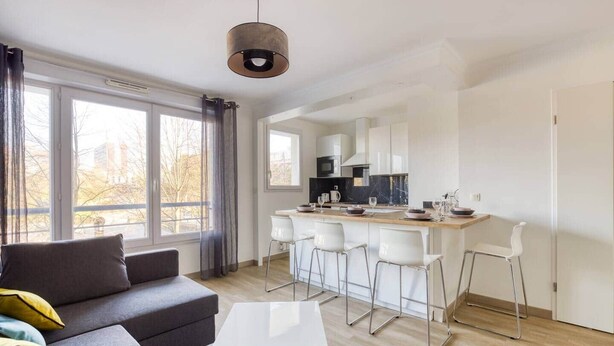 Ein modernes Wohnzimmer mit einer Couch, einem Couchtisch und einer Küchenzeile mit einer Bar und Stühlen.