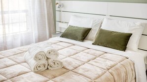 Ein ordentlich bezogenes Bett mit gesteppter Decke, zwei Kissen und aufgerollten Handtüchern an einem weißen Kopfstück.
