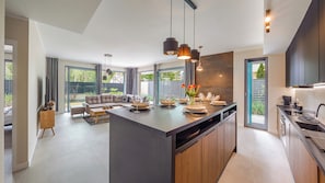 A modern kitchen with a central island, large windows, and a dining area with a sofa. - Sun & Snow Par La Mer (Rewal)