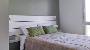 A bedroom with a bed, a nightstand, a green wall, and a window.