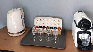 A kitchen counter with a white kettle, a coffee machine, and a tray with multiple cups and a glass.