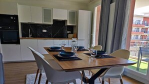 A modern kitchen with white cabinets, a black countertop, and a dining area with a wooden table and white chairs.