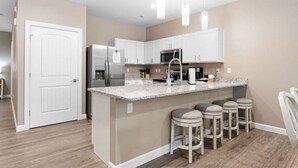 Una cocina moderna con una isla central, taburetes de bar, electrodomésticos de acero inoxidable e iluminación colgante.