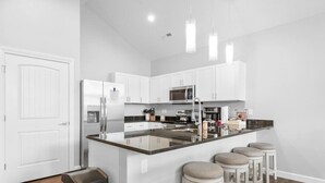 A modern kitchen with white cabinets, stainless steel appliances, and a central island with stools.