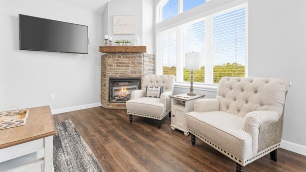 A living room with a fireplace, two armchairs, a coffee table, and a TV mounted on the wall.