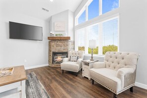 A living room with a fireplace, two armchairs, a coffee table, and a TV mounted on the wall. - Spacious 3BR | Pools, Hot Tub | Sleeps 10 (Branson)