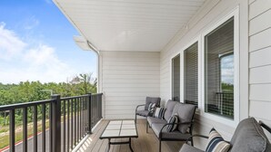 A covered porch with a wooden deck, a metal railing, and a gray sofa with striped cushions.
