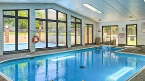 An indoor swimming pool with clear glass walls, a lifebuoy, and a warning sign.