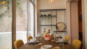 Una mesa de comedor dispuesta con platos, vasos y cubiertos, con un espejo y plantas colgantes al fondo.