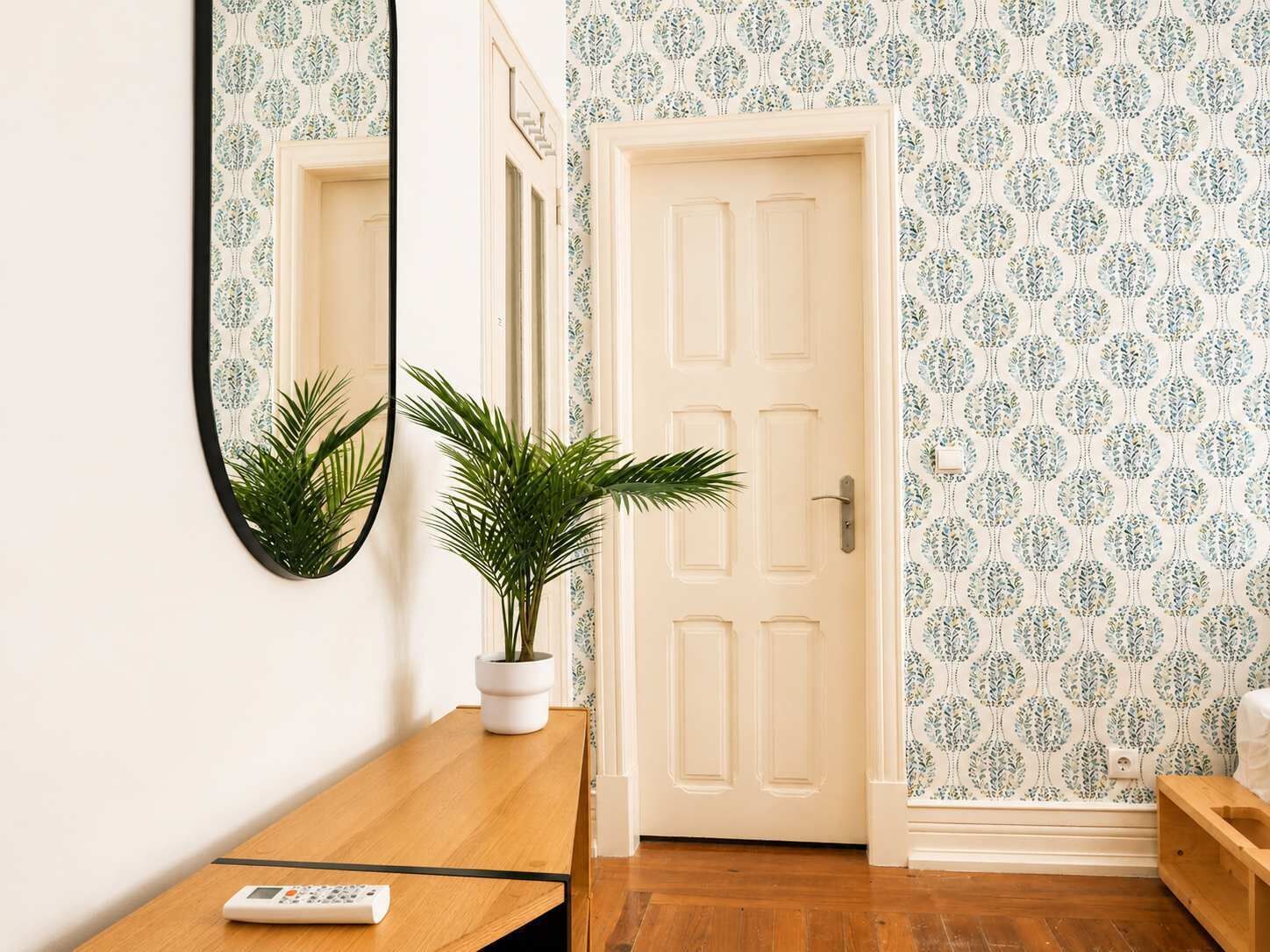 A hallway with a wooden bench, a potted plant, a door, and a mirror on the wall.