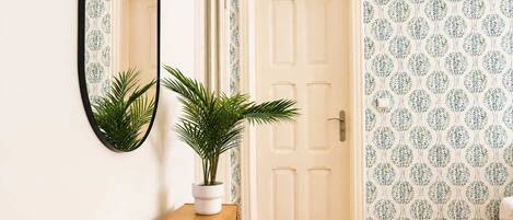A hallway with a wooden bench, a potted plant, a door, and a mirror on the wall.