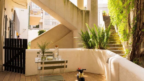 Un patio moderno al aire libre con una escalera de hormigón, una mesa pequeña con un florero y vasos, y un juguete infantil.