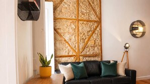 Ein modernes Wohnzimmer mit einem schwarzen Ledersofa, einem Holztisch, einem Topfpflanzen, einem gemusterten Teppich und einer ungewöhnlichen Wandgestaltung.