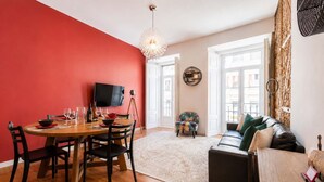 Ein Essbereich mit roter Wand, einem Holztisch und Stühlen. Ein Fernseher steht auf einem Stativ.