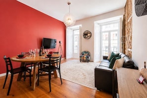 Un comedor con pared roja, una mesa de madera y sillas. Hay un televisor sobre un trípode.