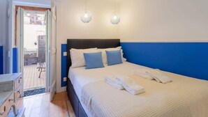 Een slaapkamer met een bed, twee wandlampen, een deur naar een buitenruimte en een kleine tafel met een stoel.
