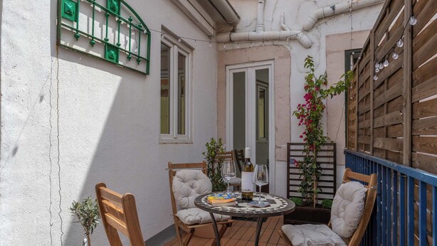 Een klein terras met een ronde tafel, twee stoelen, een plant in pot en een houten omheining.