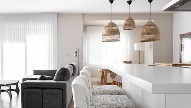 A modern kitchen with a white countertop, a grey sofa, and a dining table. There are three hanging wicker pendant lights above the kitchen island. - Grand House in the Heart of Puerto - Modern, Renovated, Near Beach, 3 Terraces, WIFI (Puerto de Sagunto)