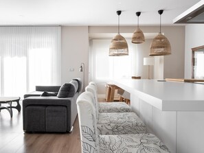 A modern kitchen with a white countertop, a grey sofa, and a dining table. There are three hanging wicker pendant lights above the kitchen island.