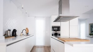A modern kitchen with white cabinetry, a wooden countertop, and stainless steel appliances including a microwave and oven. - Grand House in the Heart of Puerto - Modern, Renovated, Near Beach, 3 Terraces, WIFI (Puerto de Sagunto)