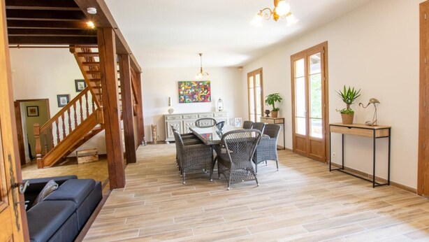 Un amplio salón con una mesa de comedor, sillas de mimbre, un sofá y una escalera.