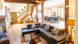 Un salón amplio con un sofá modular grande, una chimenea y una escalera de madera que lleva a un nivel superior.