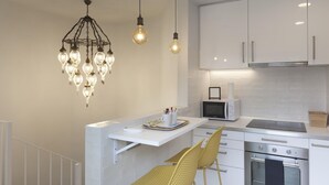 Una cocina moderna con armarios blancos, microondas integrado, estufa y lámpara colgante.