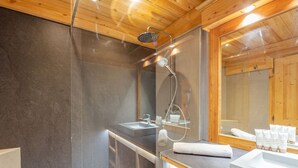 Un baño moderno con techo de madera, un espejo grande, una ducha y un tocador con lavabo y toalla.