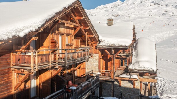 Un chalet de madera con balcón y base de piedra, rodeado de montañas nevadas.