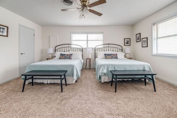 A bedroom with two beds, a ceiling fan, and a window with blinds.