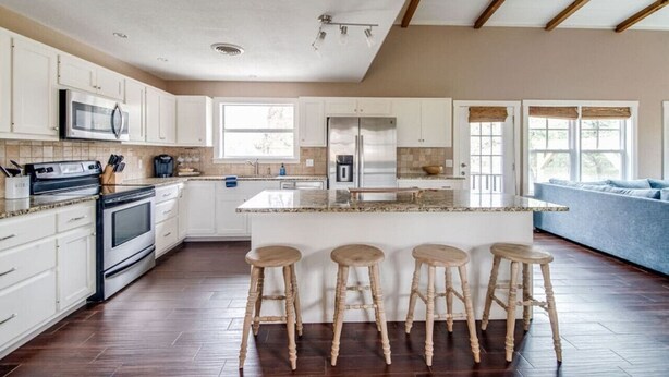 Une cuisine spacieuse avec des meubles blancs, un îlot central doté de tabourets, un four encastré et un réfrigérateur.