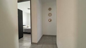 Un couloir avec un lit en arrière-plan, une porte et trois luminaires fixés au mur.