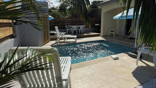 Une piscine entourée de chaises longues, de galets blancs et de palmiers.