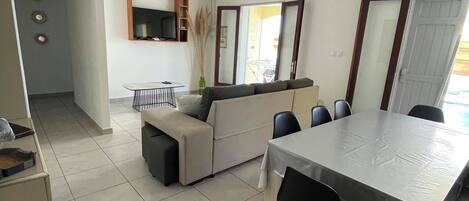 A modern kitchen with a dining area, a sofa, and a TV.