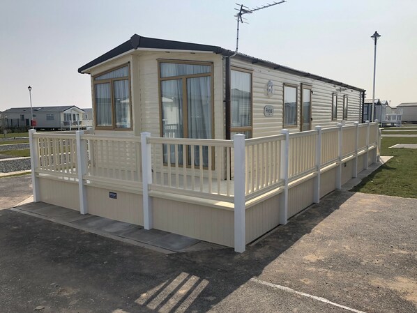 A mobile home with a fenced porch, large windows, and a satellite dish.
