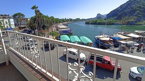 A coastal view with boats docked along the shore, a clear sky, and a mountainous backdrop.