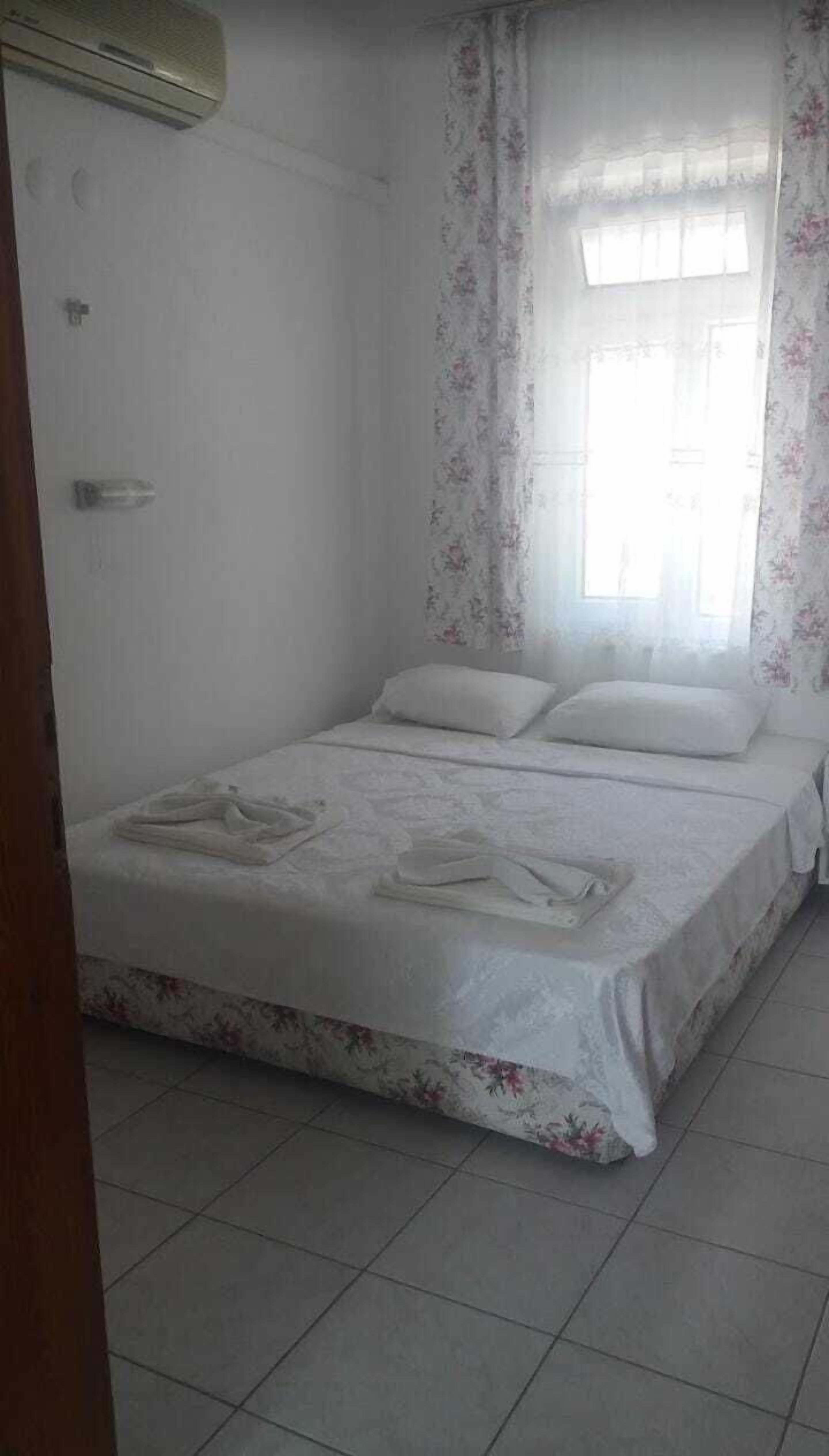 Quarto com cama, janela com cortinas florais e piso ladrilhado.