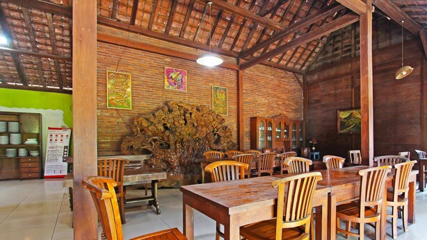A wooden dining area with tables and chairs, a brick wall with artwork, and a ceiling with exposed beams. - Hotel O Kopi Klotok Homestay Syariah (Secang)