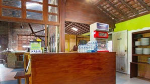 A restaurant interior with a wooden reception desk, a visible toilet, and a shelf with plates. - Hotel O Kopi Klotok Homestay Syariah (Secang)