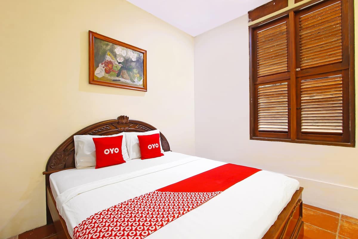 Un letto ben rifatto con copriletto rosso e bianco, due cuscini con la scritta "OYO" e un quadro appeso sopra il letto.