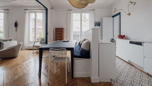 Un salon moderne comprenant une table à manger, un canapé blanc et un coin cuisine avec des meubles blancs et un lave-vaisselle.