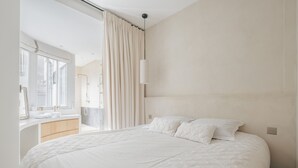 Une chambre moderne avec un grand lit, une salle de bain équipée d’un meuble-lavabo et une vue sur l’extérieur.